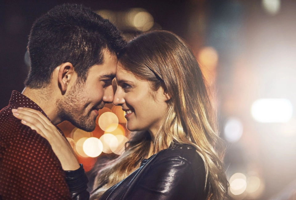 A couple standing forehead to forehead under city lights at night