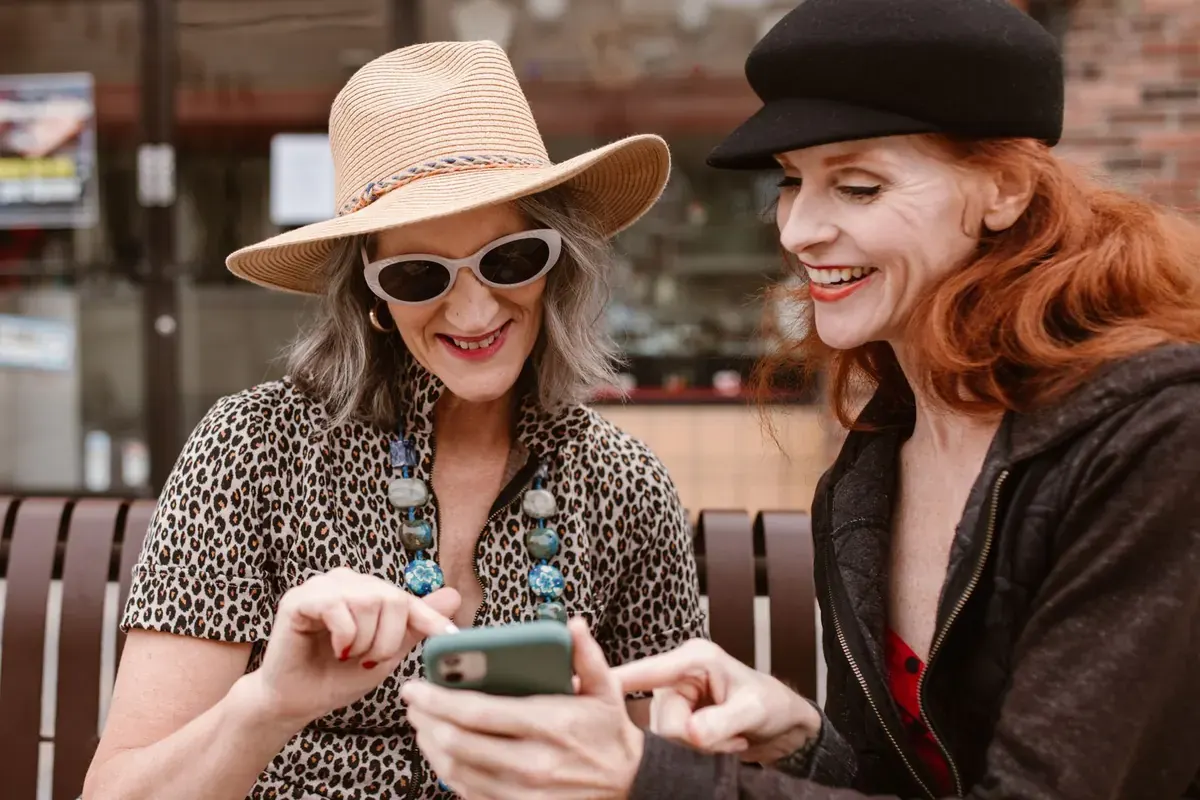 Two women in hats laughing as they look at a phone together