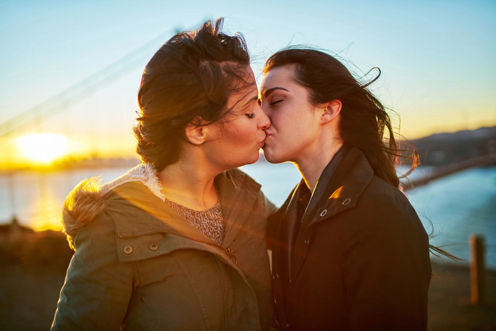 Two women kissing by the water as the sun sets