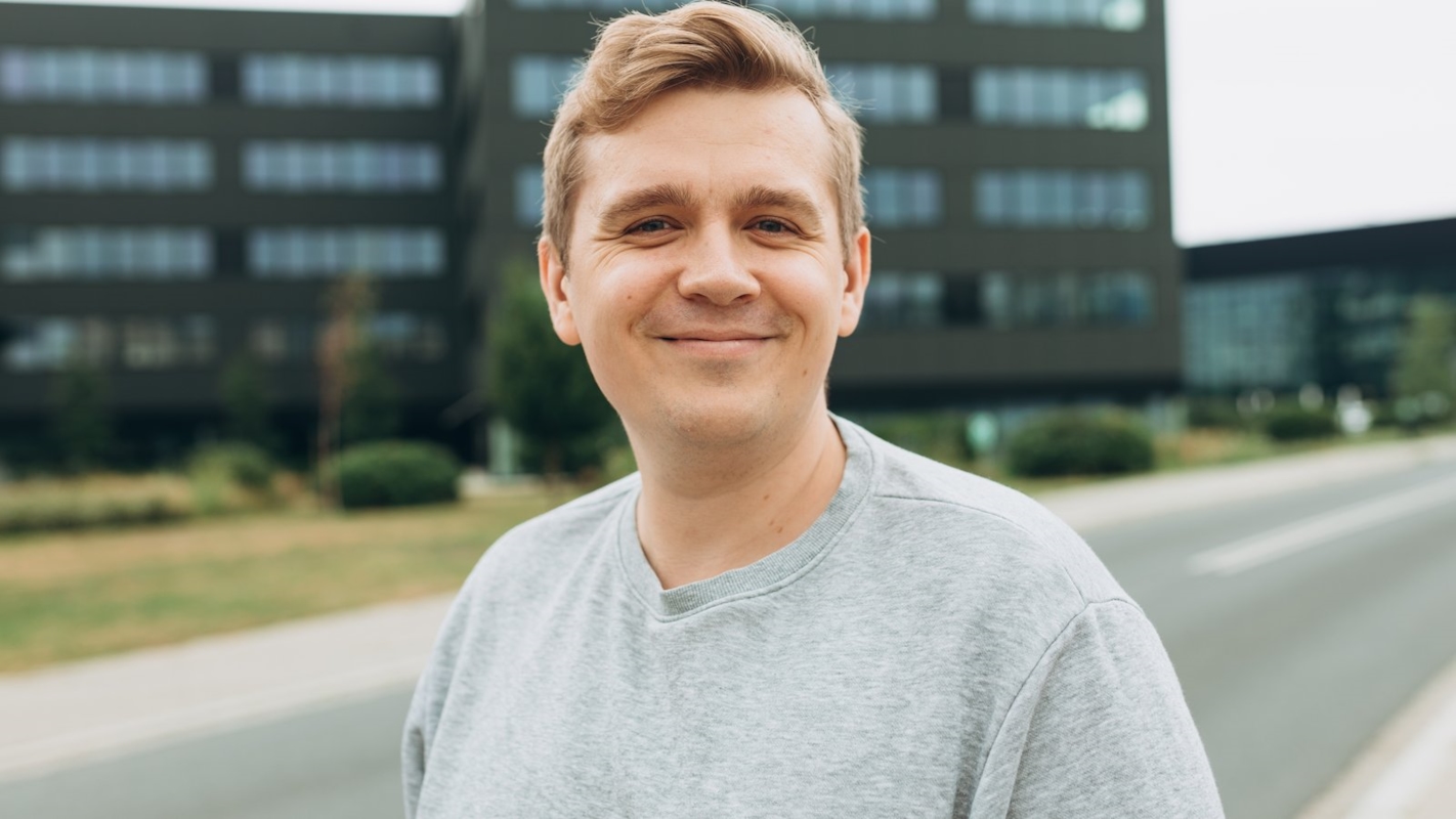 A man smiling outdoors near an office building