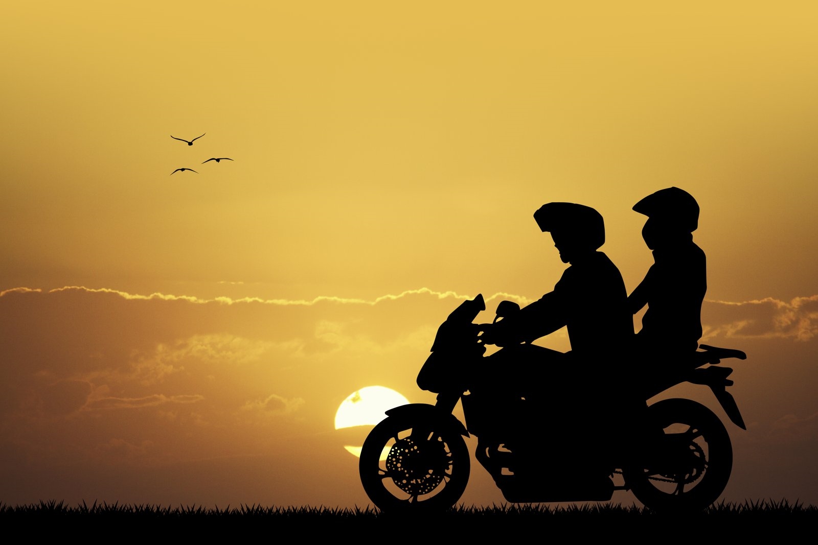 Silhouette of a biker and pillion riding into the sunset