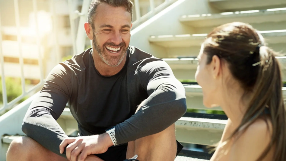 A smiling man in his 40s chatting with a woman on outdoor stairs after a workout