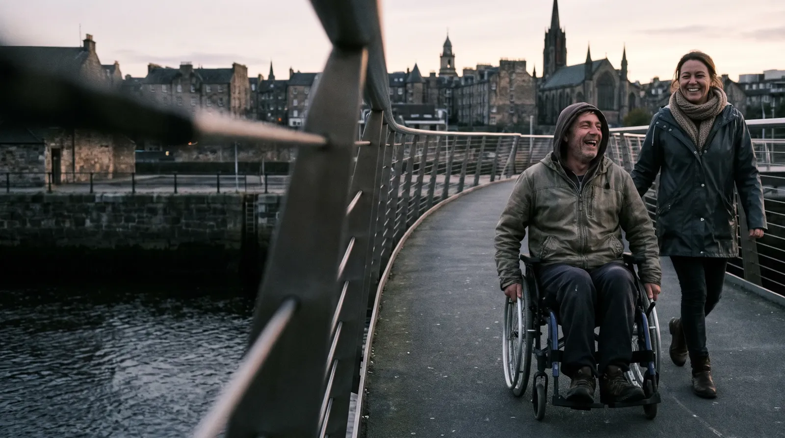 A couple laughing on the Peace Bridge in Derry at dusk; the man is a wheelchair user
