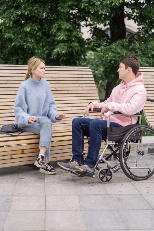 A man in a wheelchair and a woman talking together on a park bench