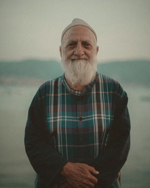 Older man with a white beard smiling by the water