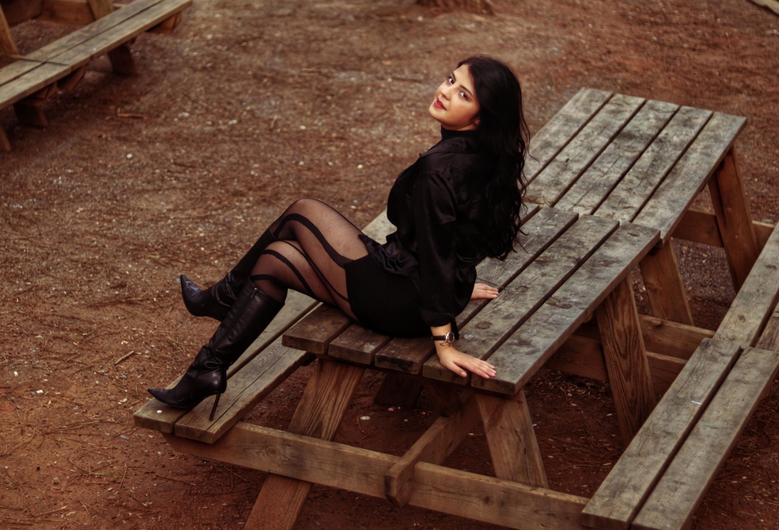 Confident dark-haired woman in a black date outfit and patterned stockings outdoors