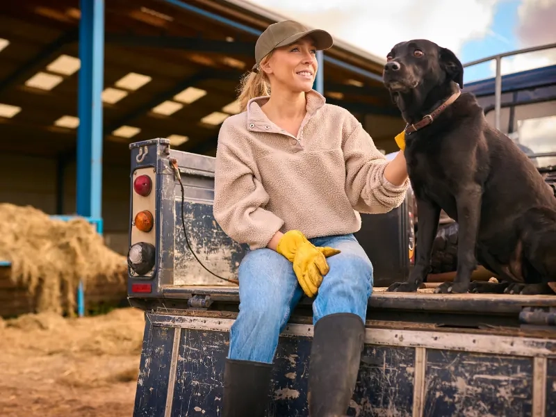 A woman sitting on a trailer with her dog in a barn
