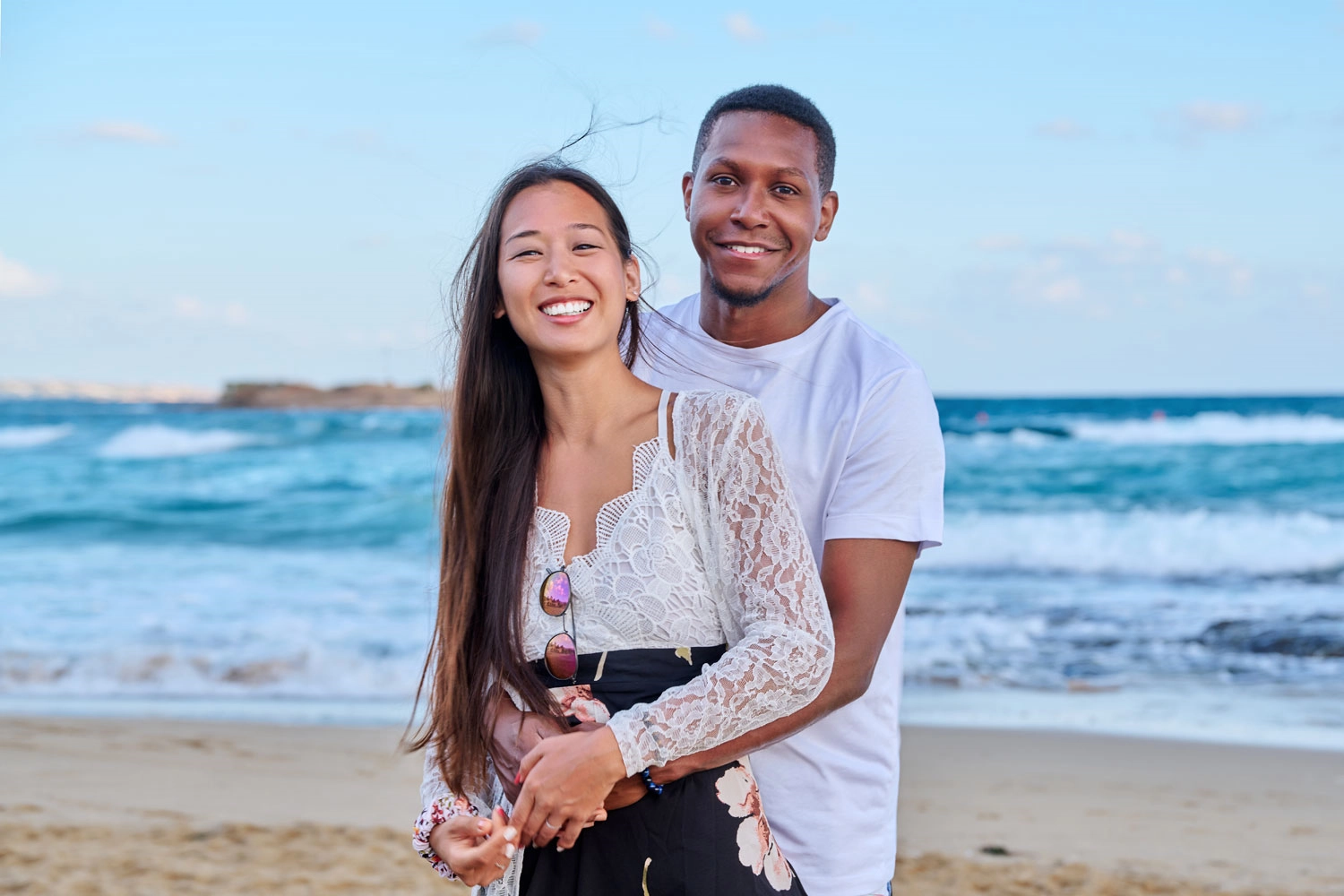 A couple posing together on a beach with the sea behind them