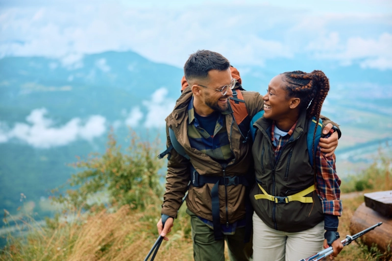 A laughing man and woman hiking arm in arm above a misty valley