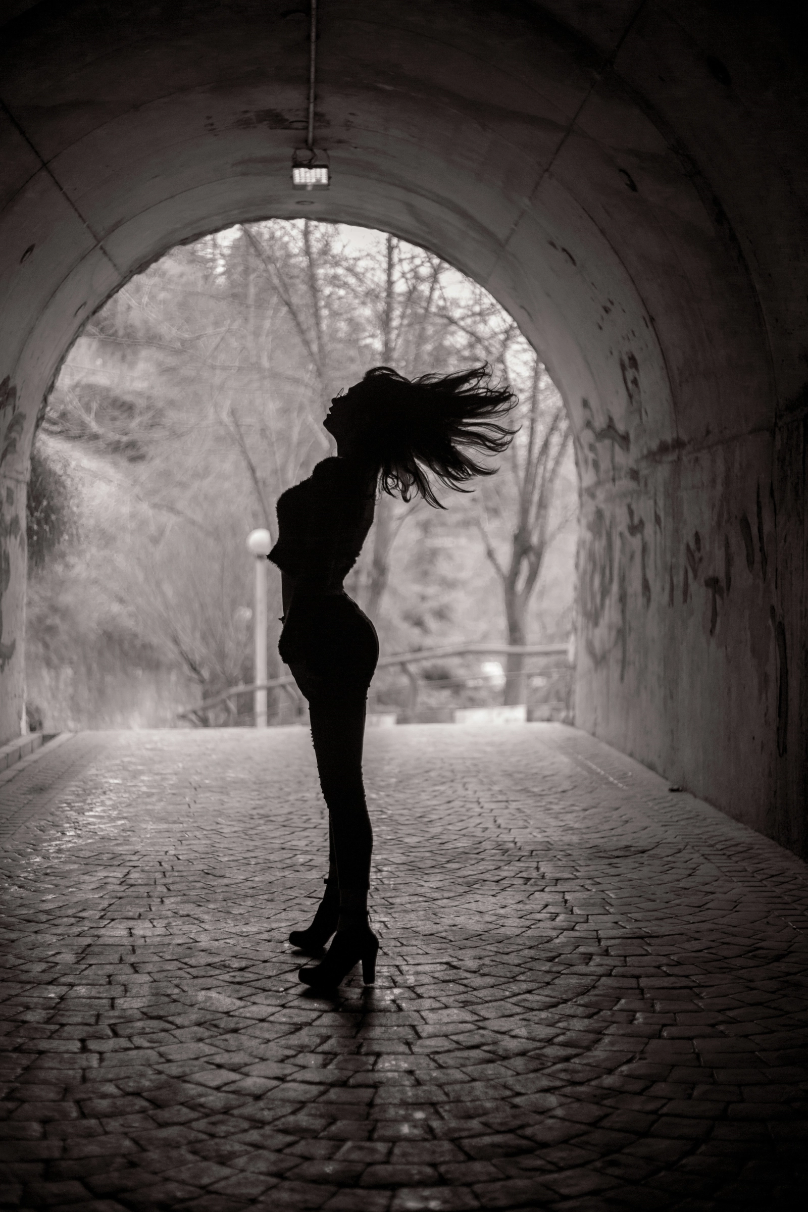 Silueta en blanco y negro de una persona con tacones y el pelo en movimiento, en un túnel de piedra