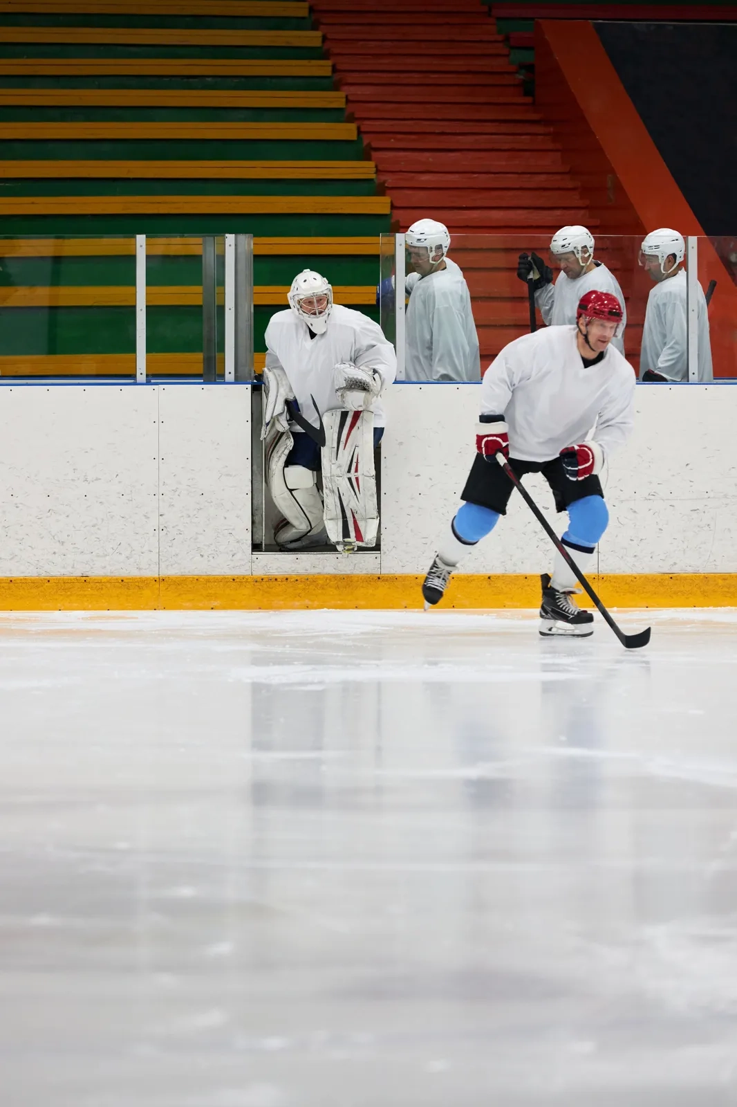 Goalie in white gear and a skater on a brightly lit indoor rink