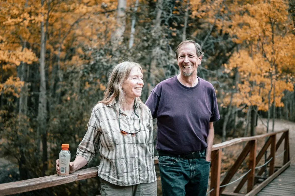 A couple laughing together on a wooden footbridge among autumn trees