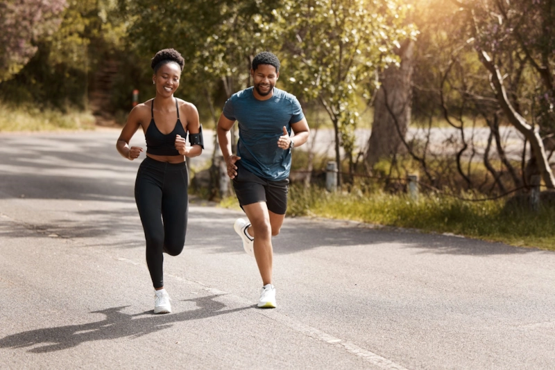 A woman and man running side by side along a sunny tree-lined road