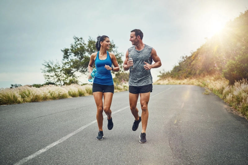 A smiling woman and man jogging together along a quiet road