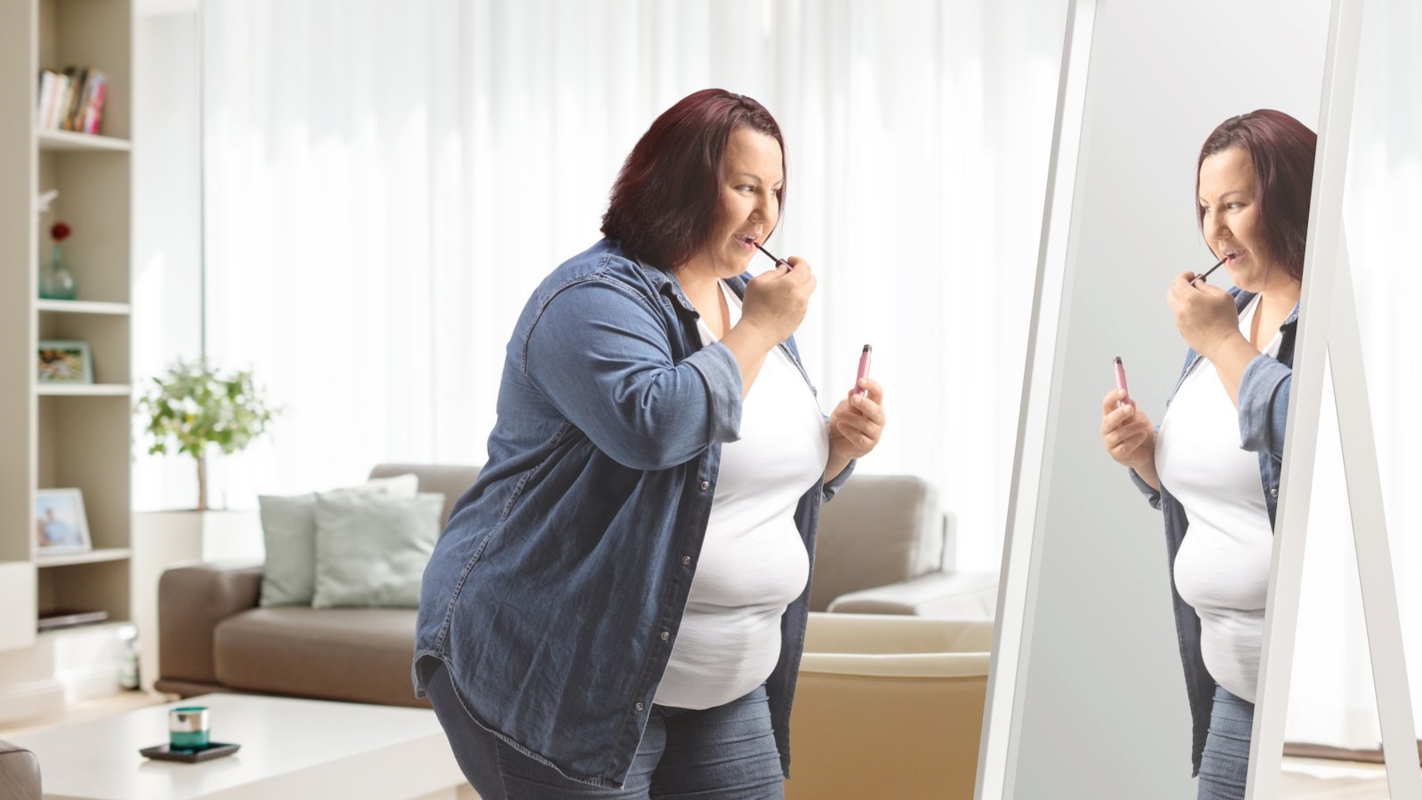 A woman applying lipstick in front of a mirror at home while getting ready