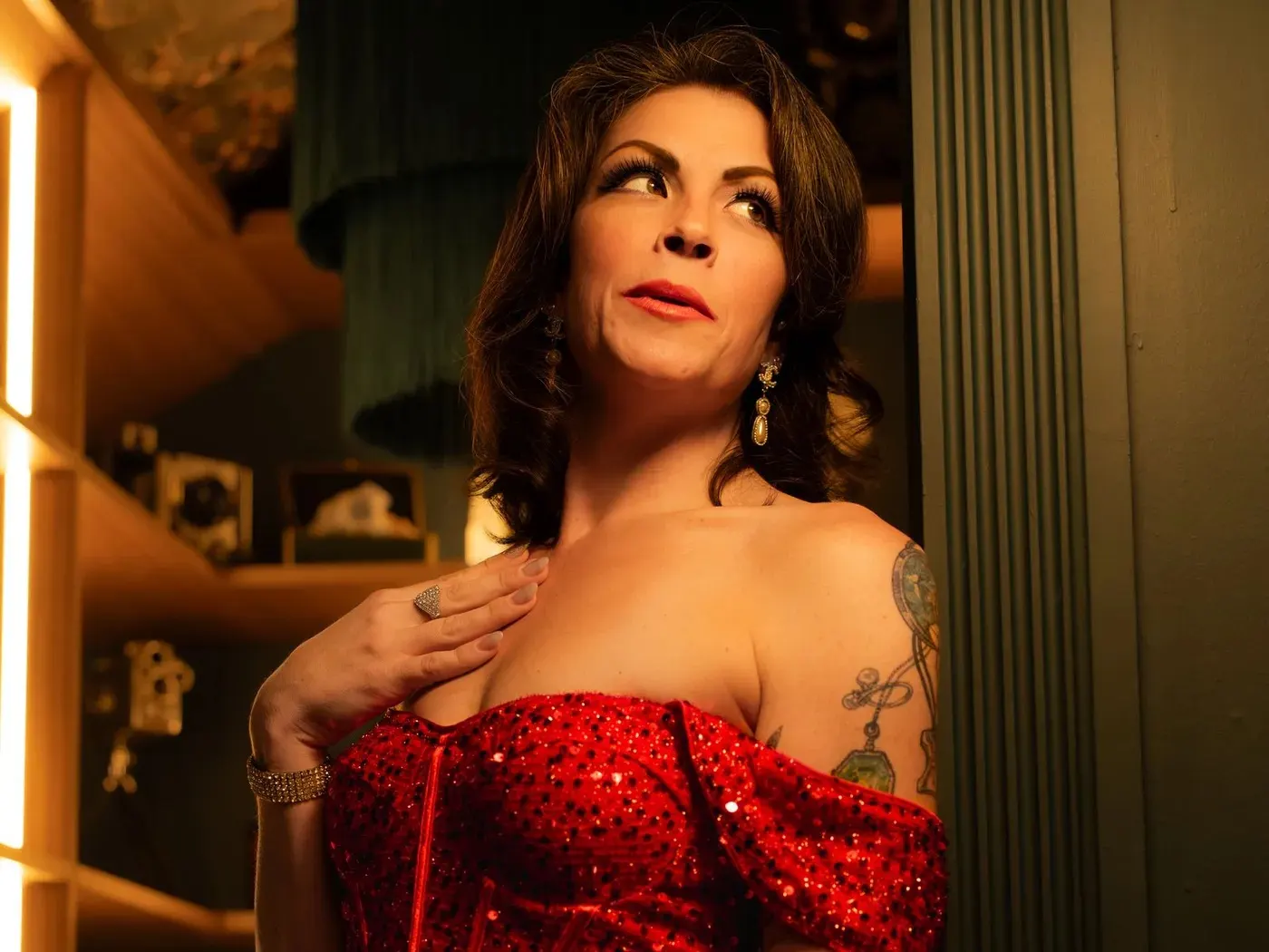 A dark-haired woman in an off-the-shoulder red sequinned dress glancing over her shoulder in warm low evening light