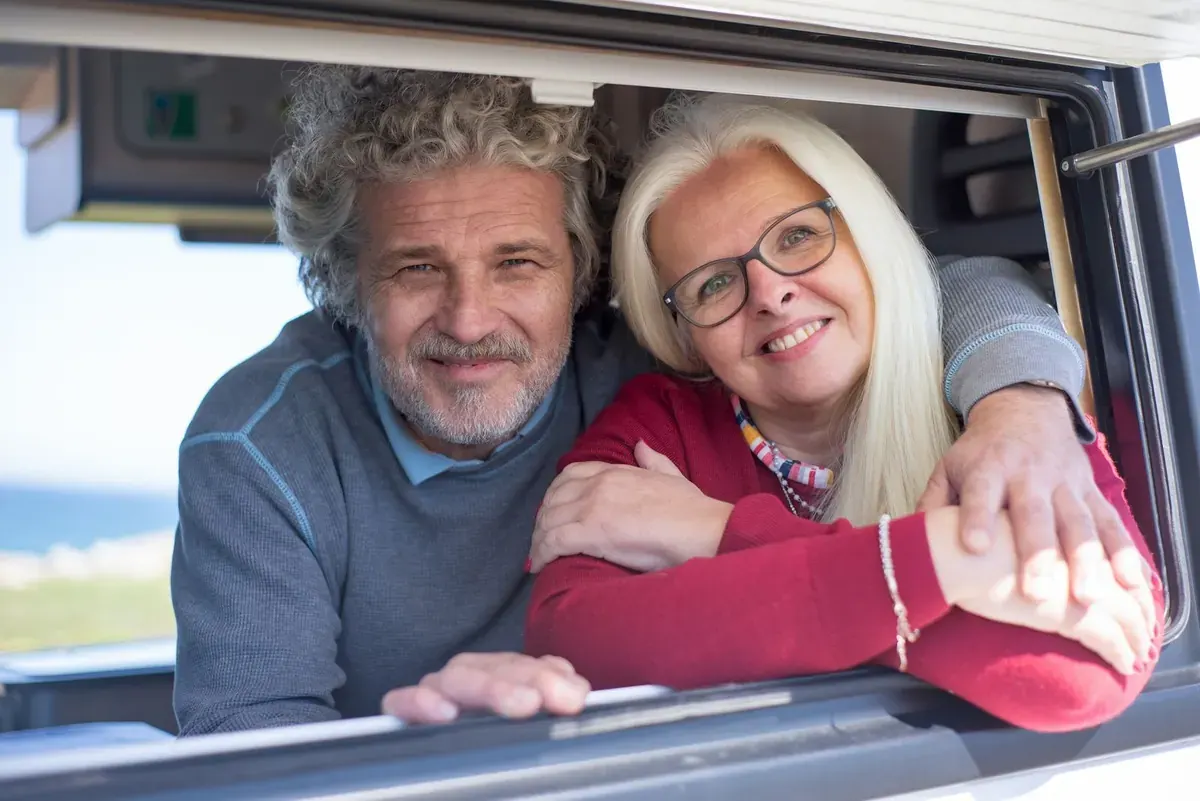 A laughing couple leaning out of their campervan window on a road trip