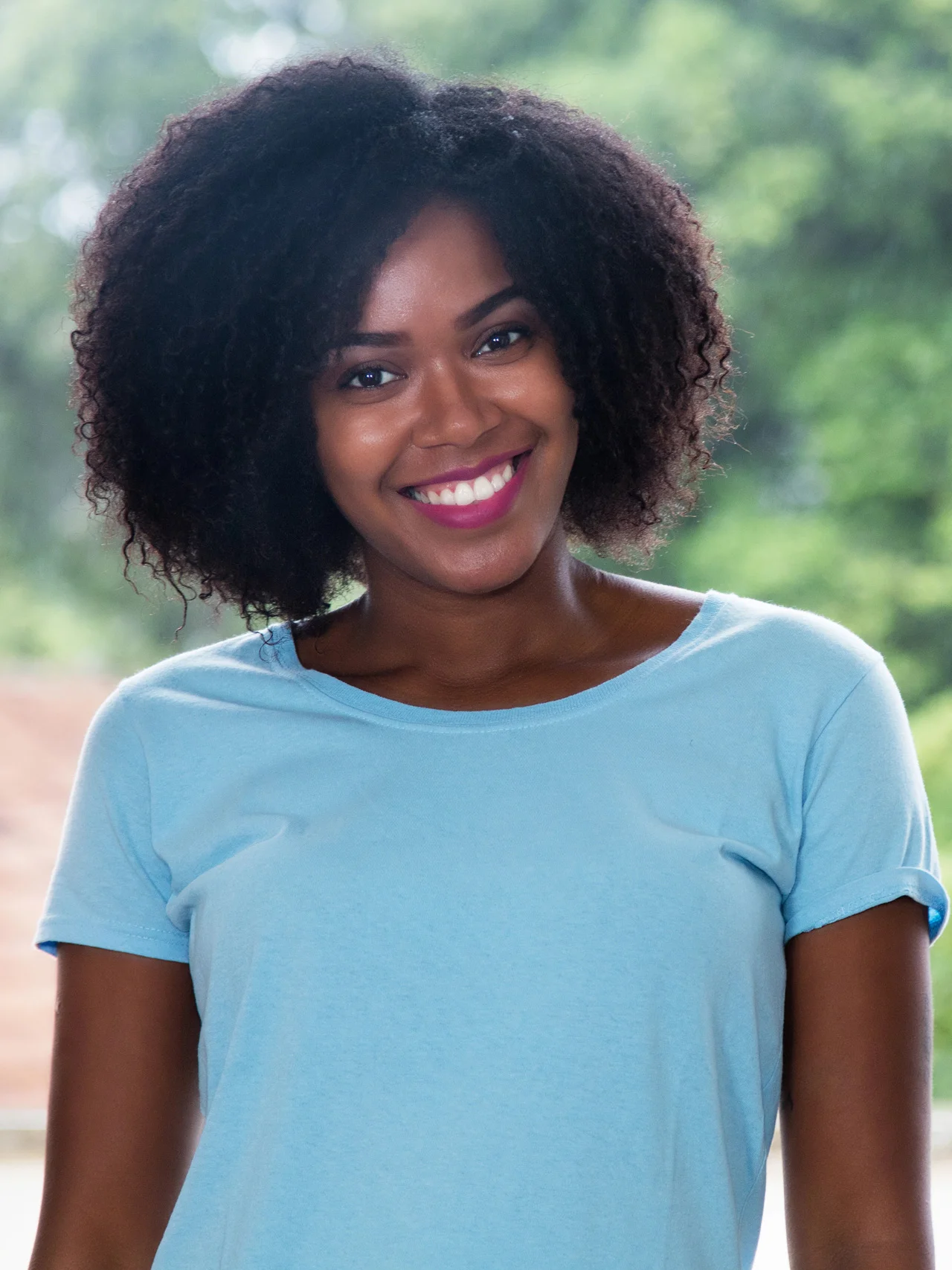 A smiling woman with natural curly hair in a light blue t-shirt