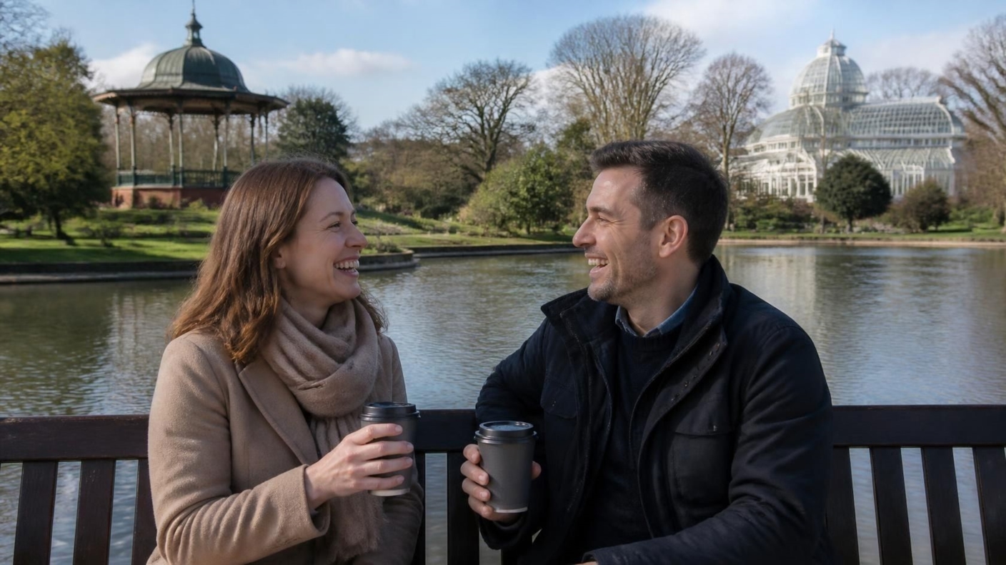 A couple laughing over takeaway coffees on a bench beside a lake in a park