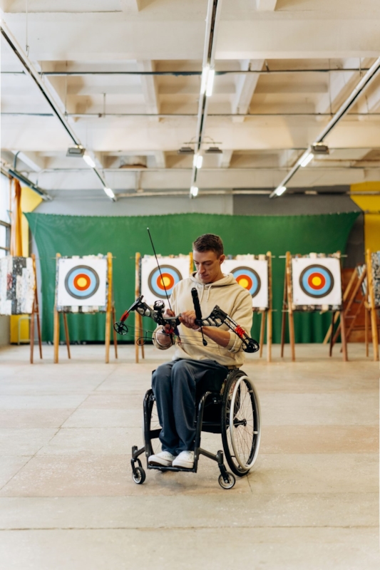 A man in a wheelchair holding a bow at an indoor archery range