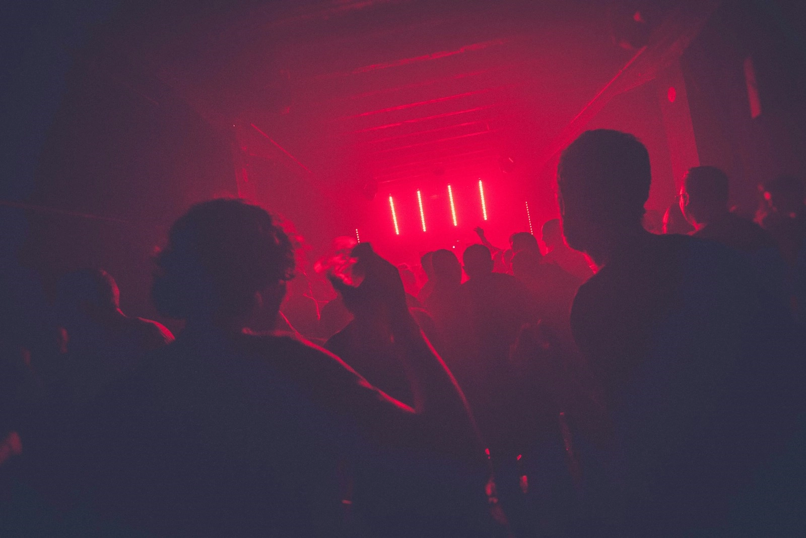 A crowd in silhouette under red lights at a club night