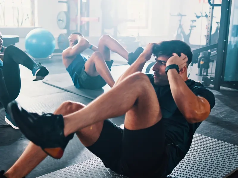 A fitness class doing bicycle crunches on mats in a bright studio