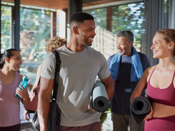 A group of friends of different ages chatting and laughing with yoga mats after class