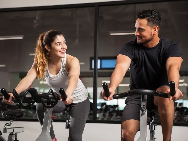 A man and woman smiling at each other from neighboring bikes in a spin class