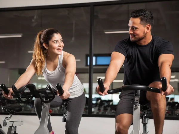 A man and woman smiling at each other from neighboring bikes in a spin class