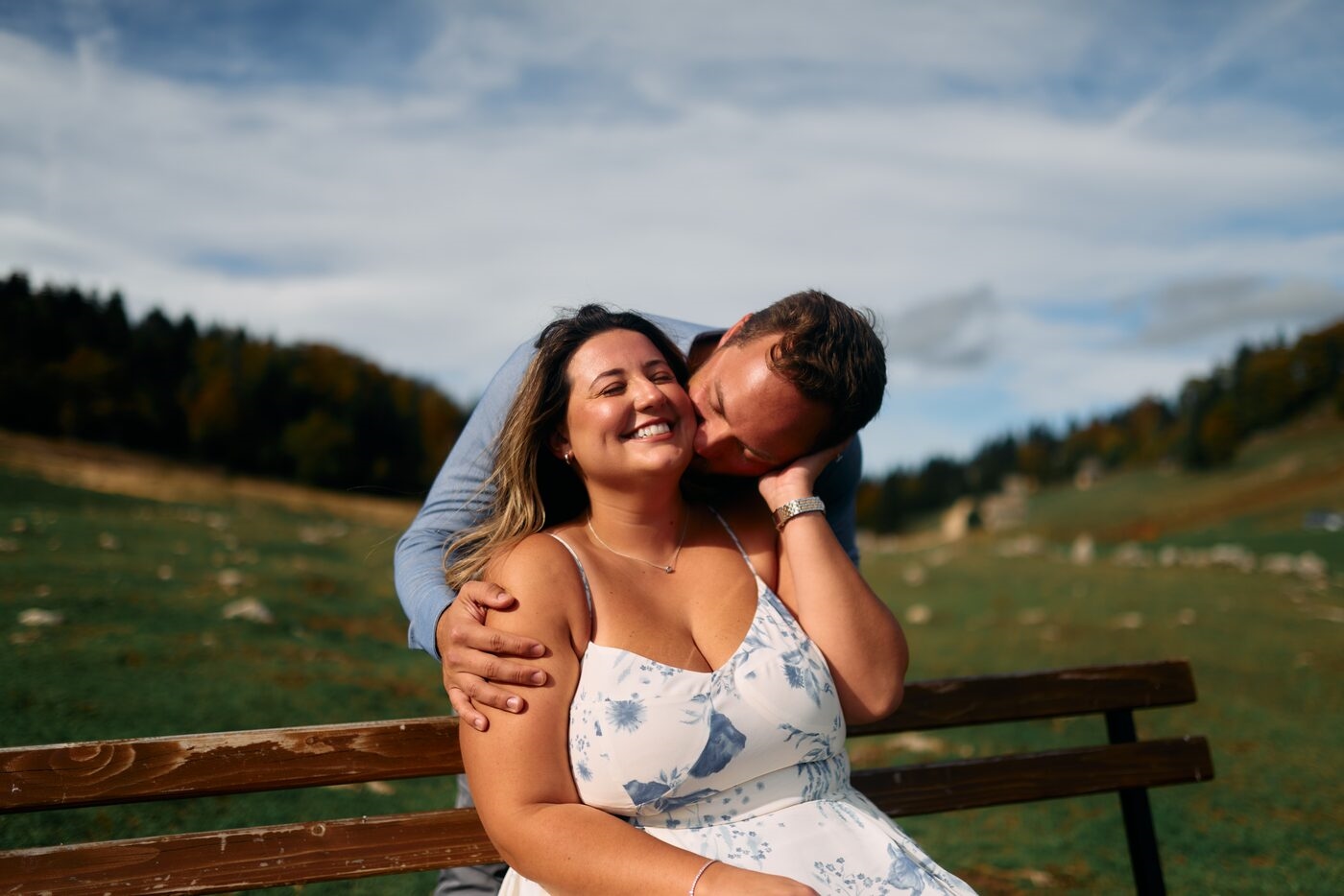 A couple sitting close together on a park bench outdoors, sharing a warm, joyful moment in the sunshine