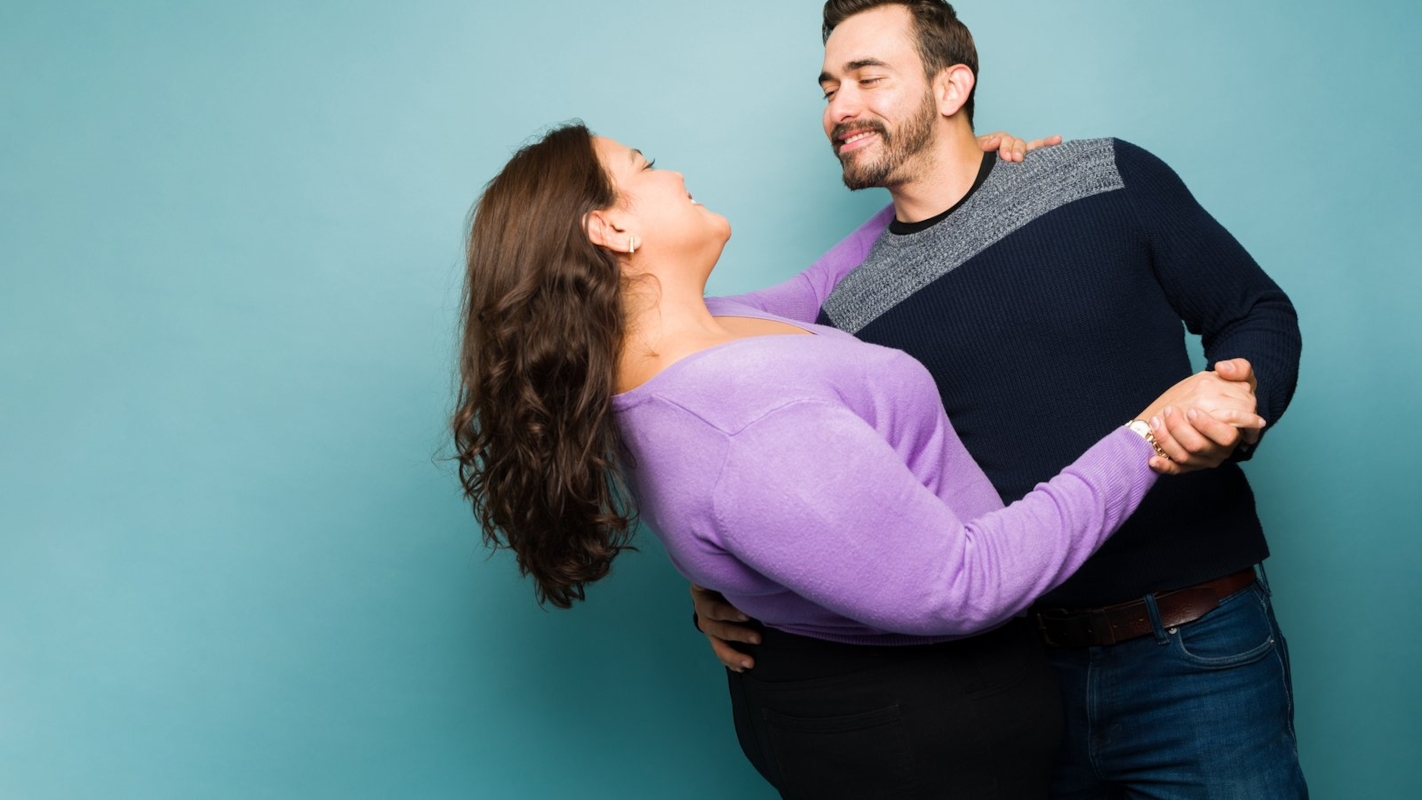 A couple laughing together, him holding her in a playful dip