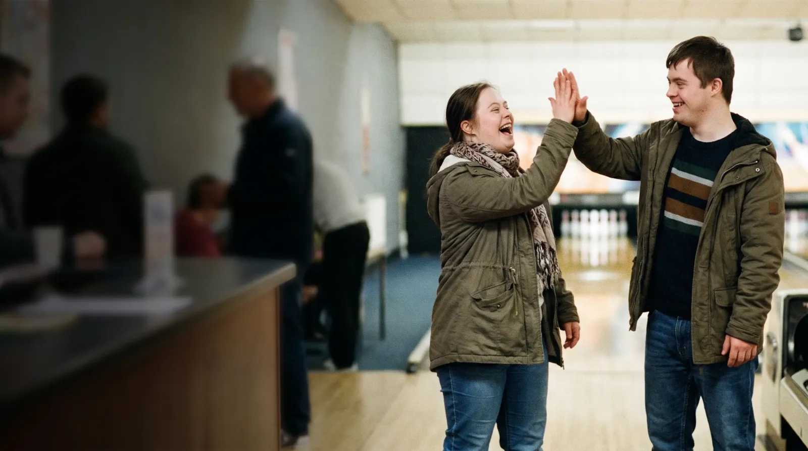 A young couple who both have Down syndrome sharing a laughing high five at a bowling alley