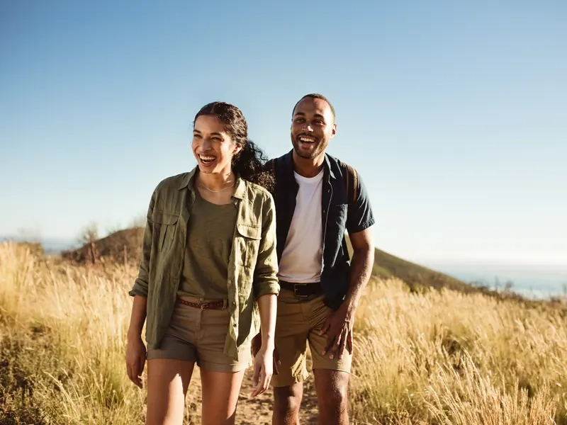 A laughing couple walking through golden grass on a sunny hillside