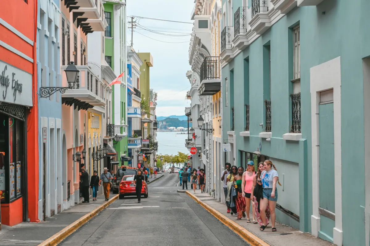 Una calle en cuesta del Viejo San Juan, con fachadas de colores y gente caminando por la acera.