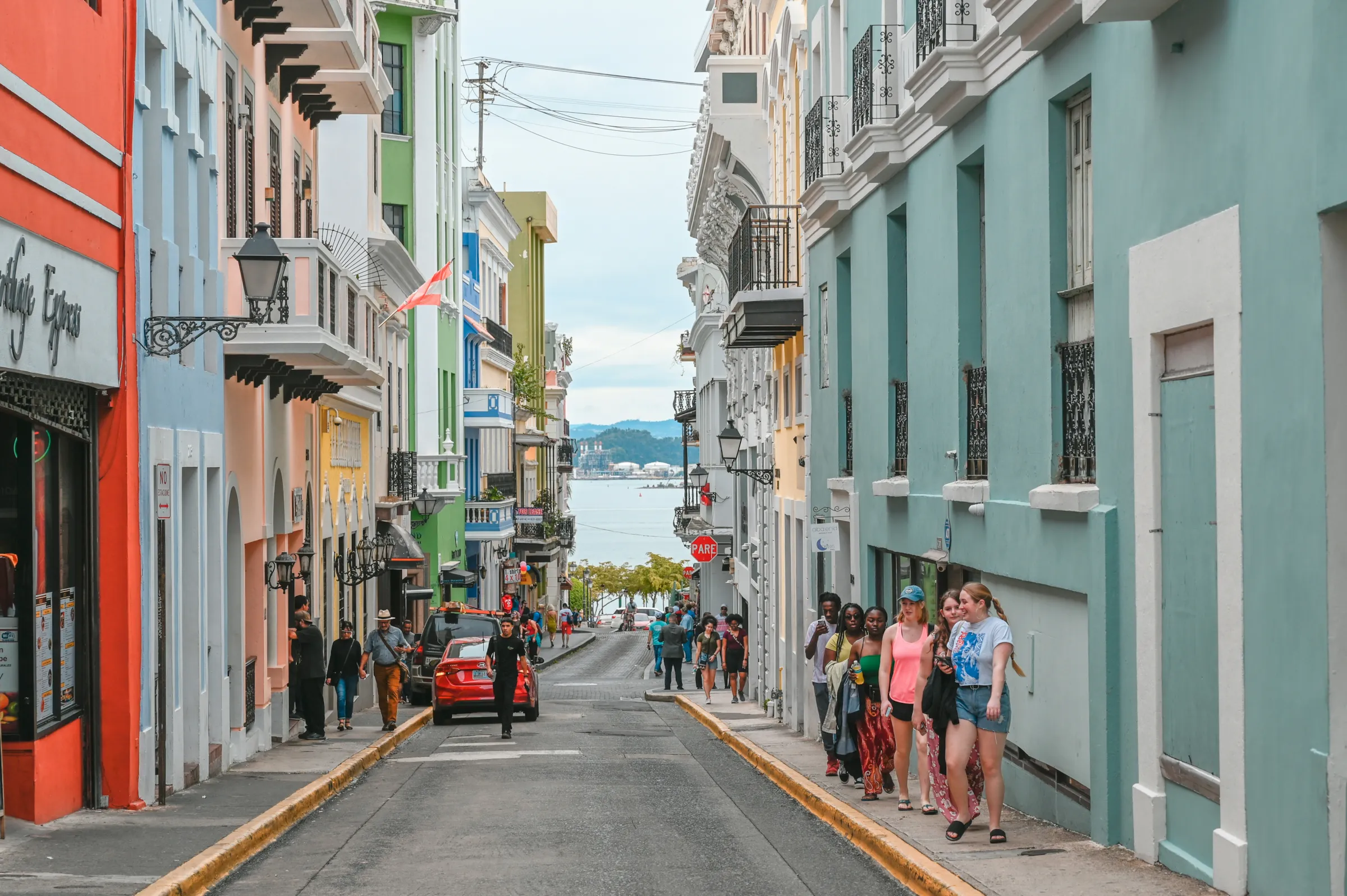Una calle en cuesta del Viejo San Juan, con fachadas de colores y gente caminando por la acera.