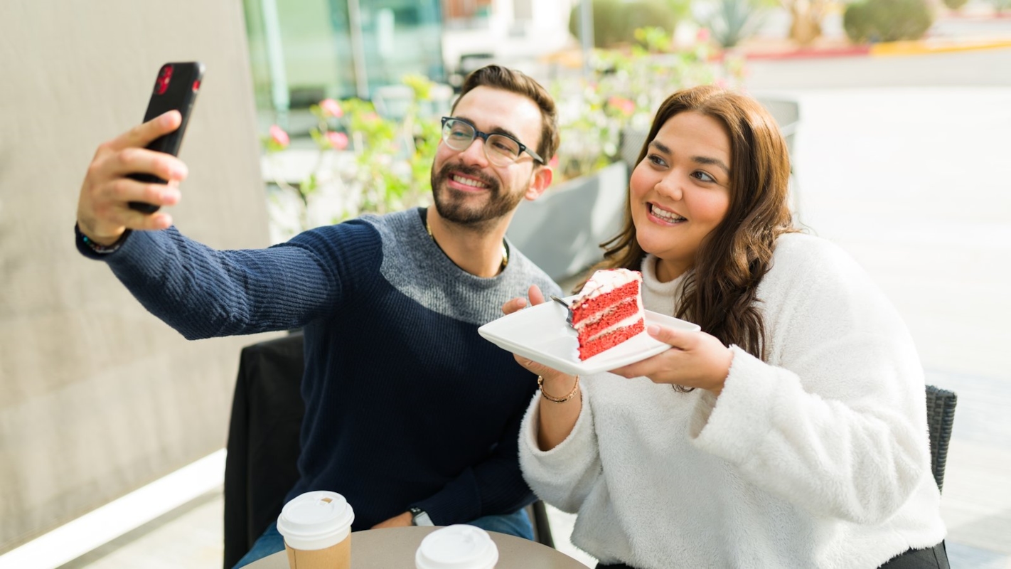 A couple taking a selfie together at a cafe, sharing a slice of cake