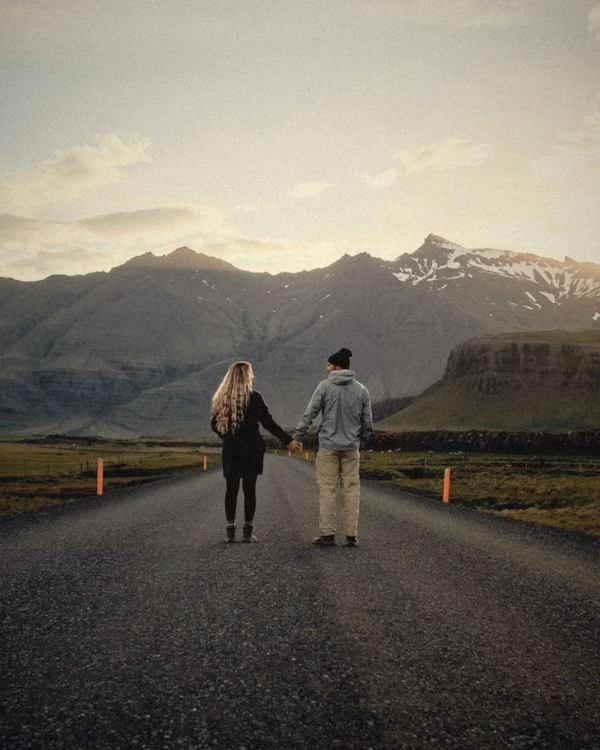 Couple walking hand in hand down an open road towards mountains