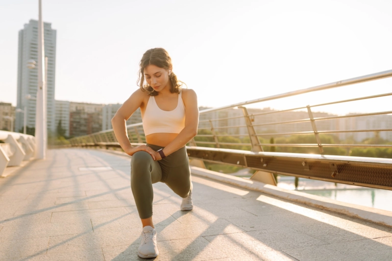 A woman stretching in a lunge on a city footbridge at sunrise