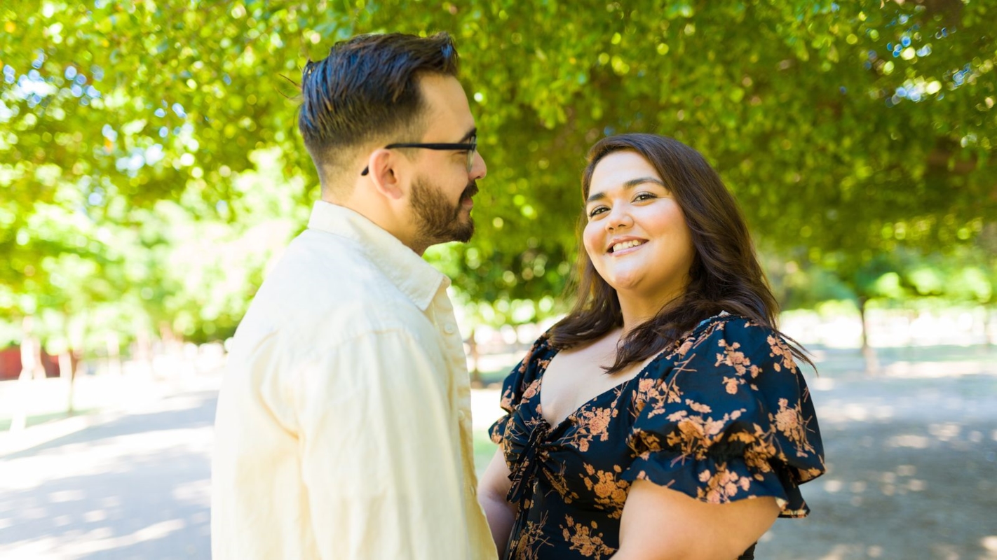 A couple smiling at each other on a tree-lined path
