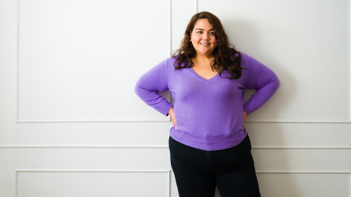 A woman standing confidently against a wall, smiling