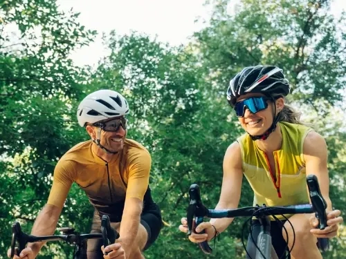 A smiling man and woman road cycling side by side through a leafy park