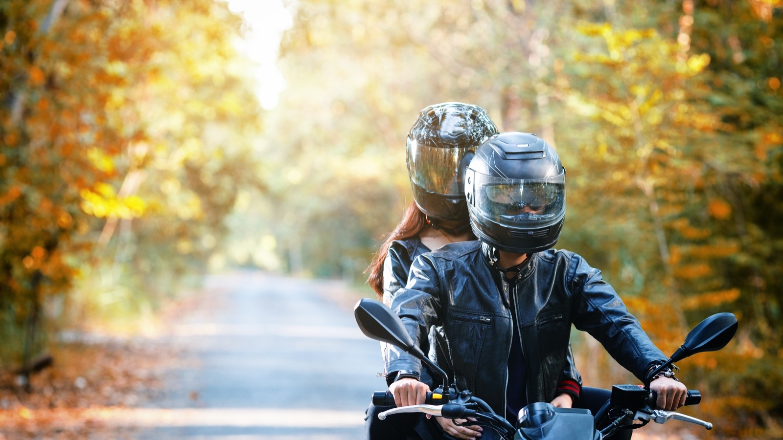 A rider and pillion riding along a quiet road lined with autumn trees