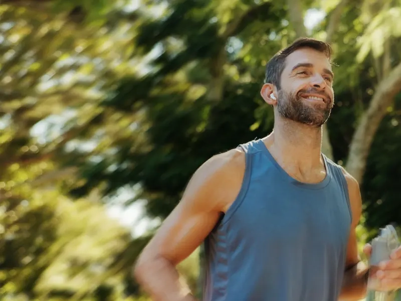 A smiling man running along a tree-lined path