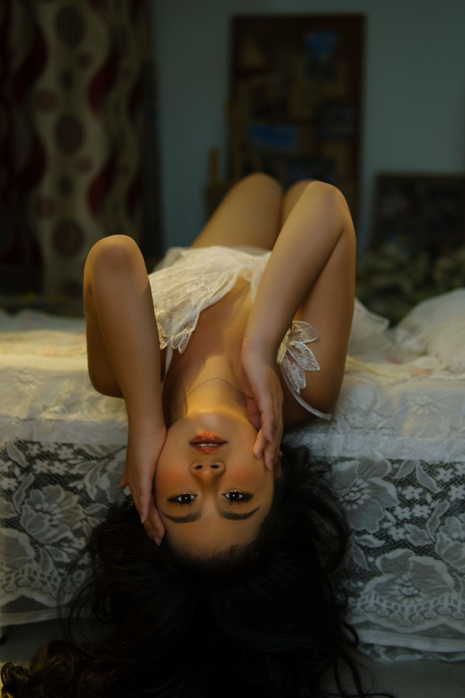 Illustrative stock. Woman in white lace lingerie lying upside down on a bed in a warmly lit bedroom.
