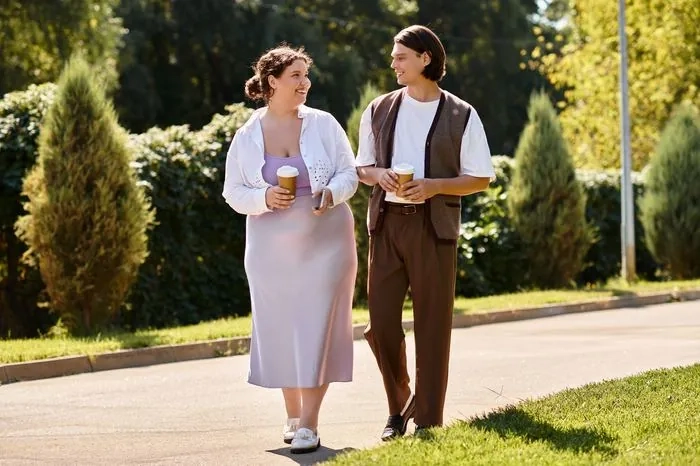 A curvy couple walking together on a first date, laughing and holding coffee
