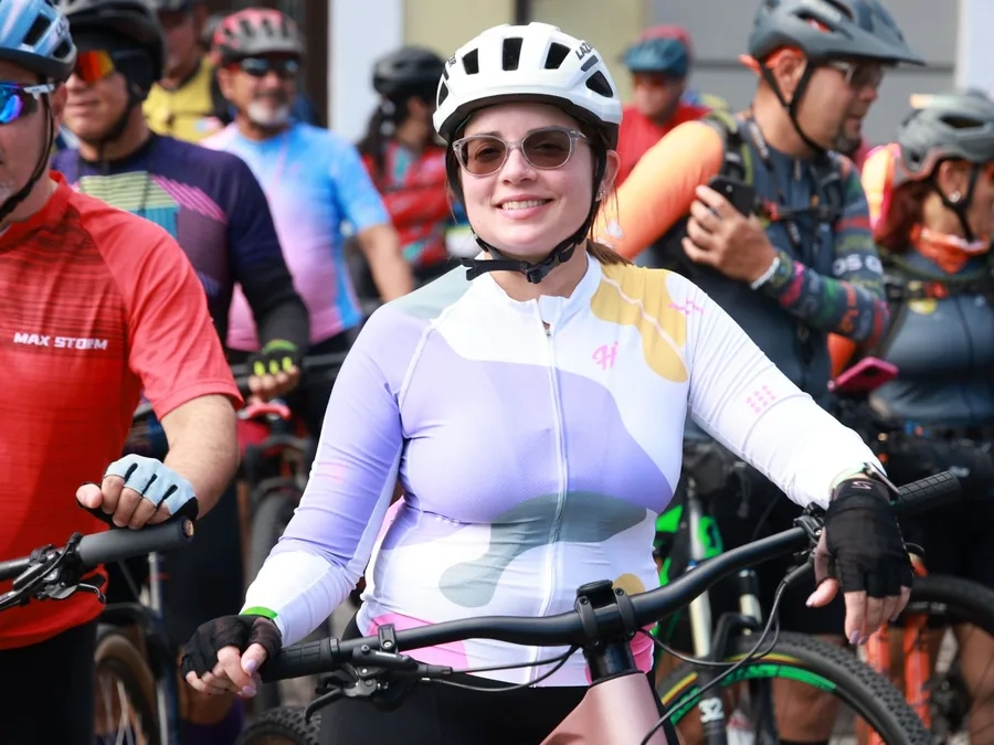 A smiling woman in a white helmet and colourful cycling jersey among a group of riders on a sunny day