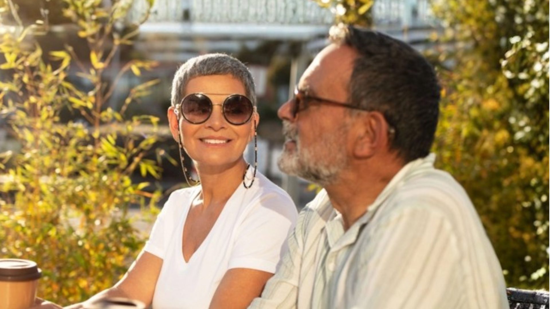 A widowed couple sitting outside together, smiling and sharing coffee