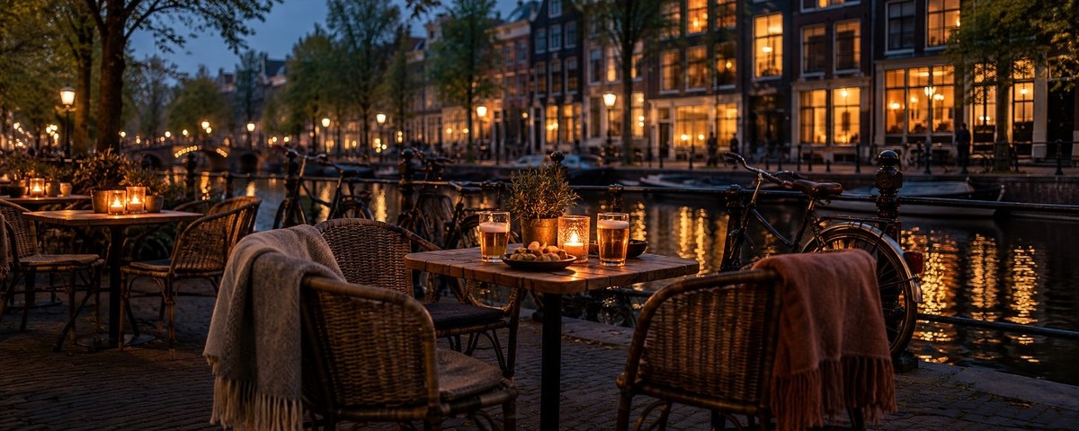 A candlelit canal-side terrace with blankets on the chairs and bicycles along the railing at dusk