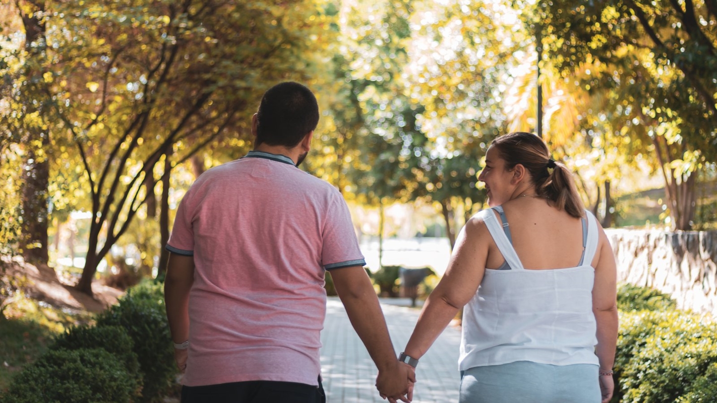 A couple walking hand in hand outdoors along a tree-lined path