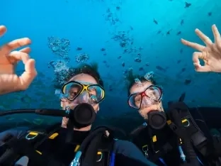 A couple scuba diving together, giving OK signs to the camera underwater